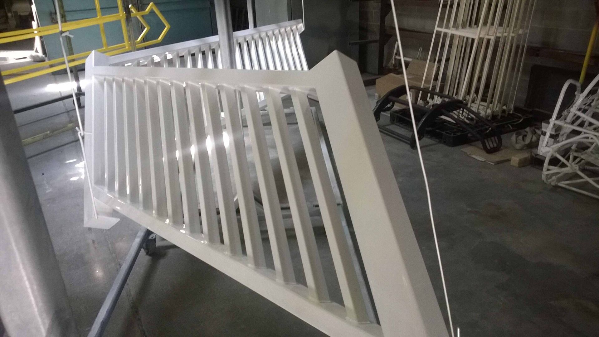 A white railing is being painted in a factory.