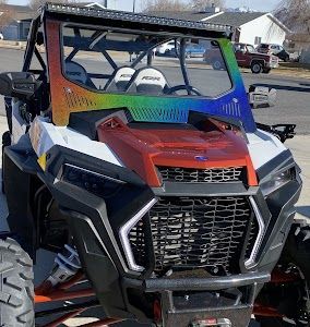 A red and white atv with a rainbow windshield is parked on the side of the road.