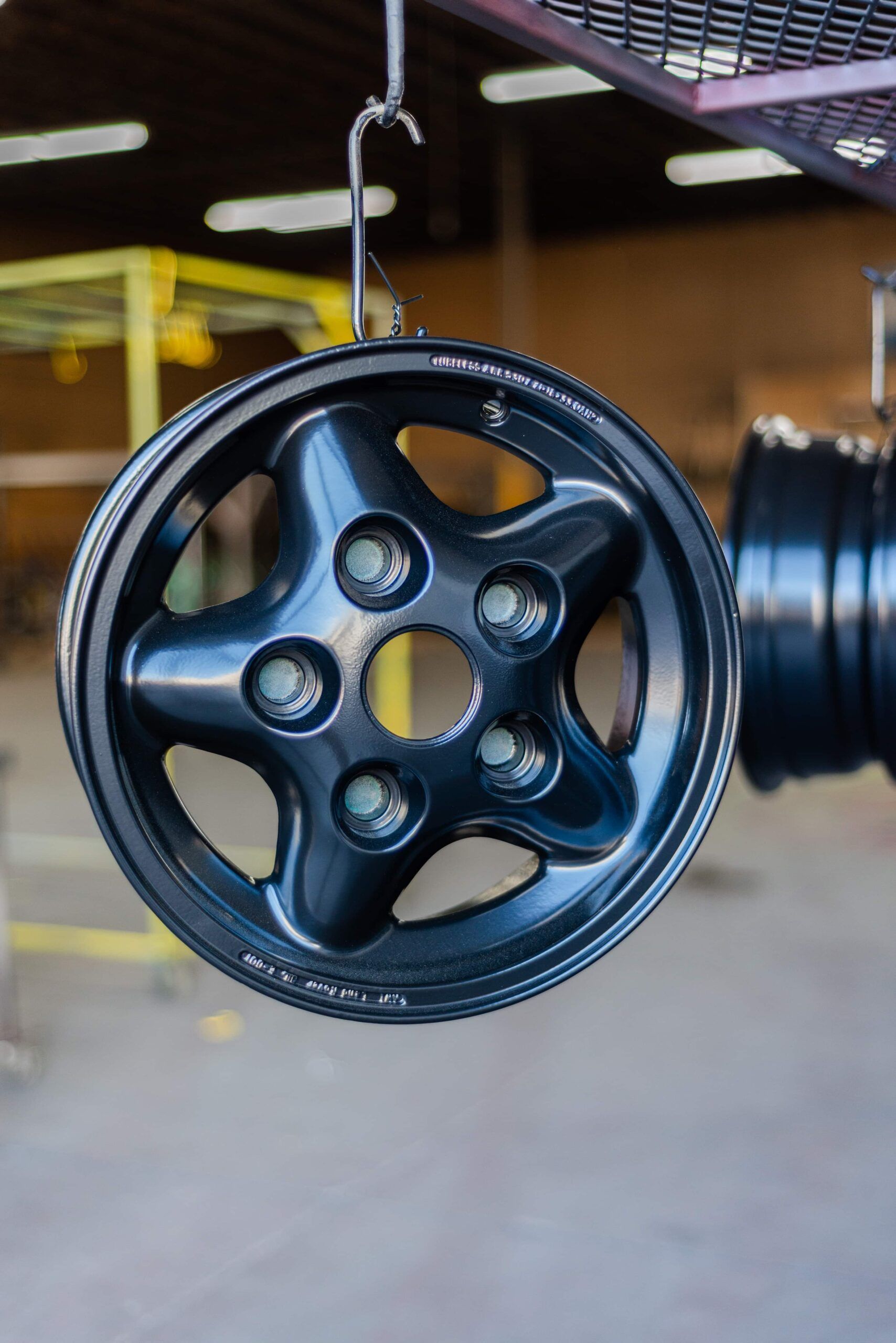A black wheel is hanging from a hook in a warehouse.