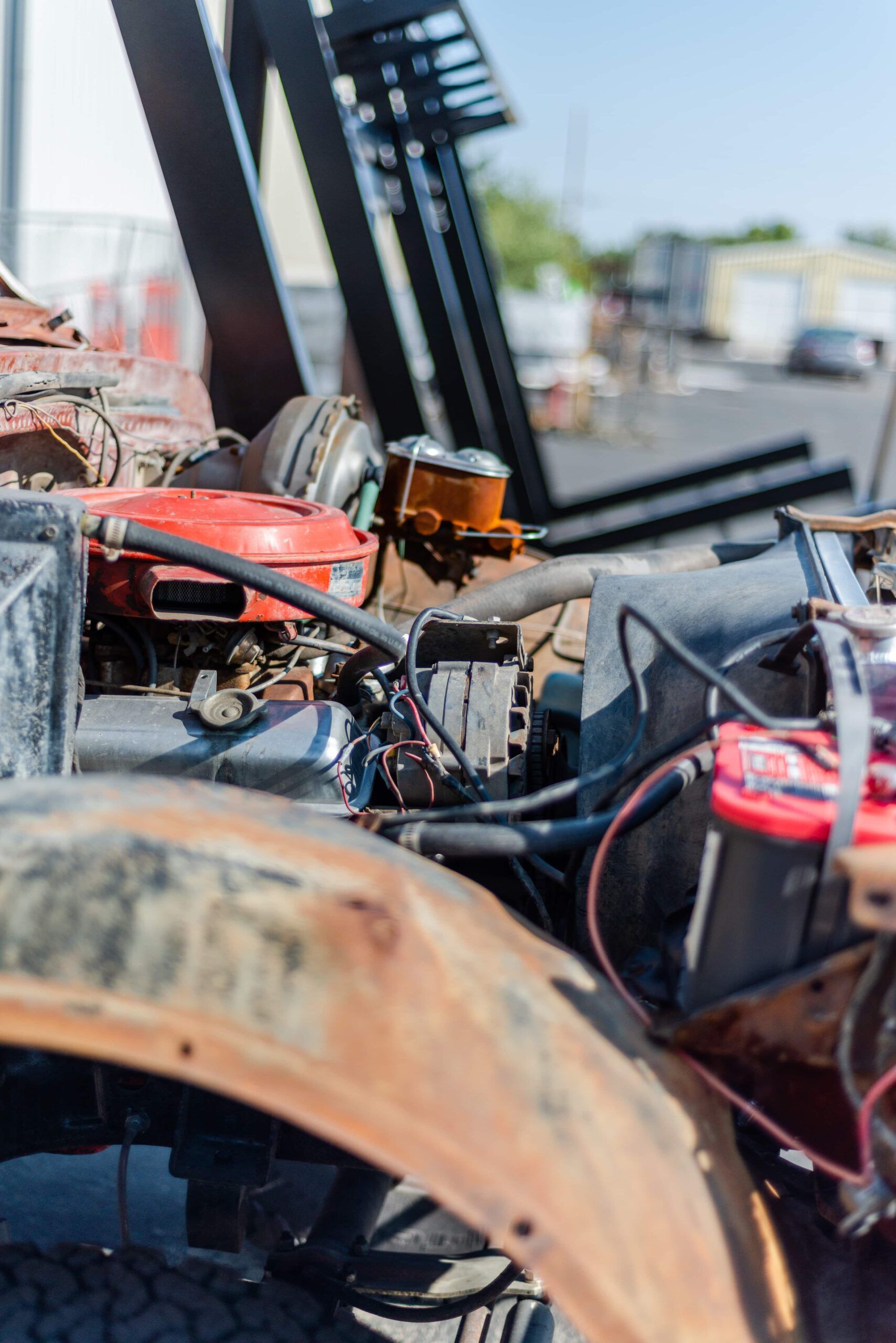 A close up of the engine of an old rusty truck with a forklift in the background.