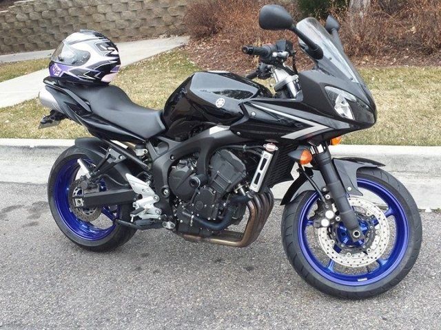 A black motorcycle with blue wheels is parked on the side of the road