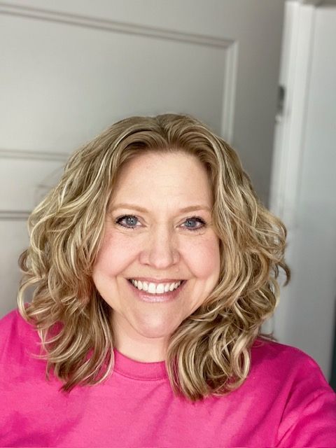 The woman is wearing a pink shirt and smiling for the camera.