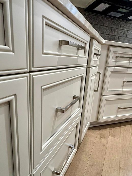 A kitchen with white cabinets and drawers with stainless steel handles.