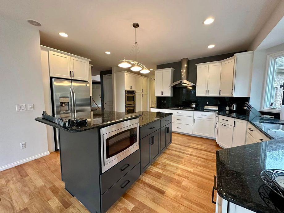 A kitchen with a large island , stainless steel appliances , granite counter tops and white cabinets.