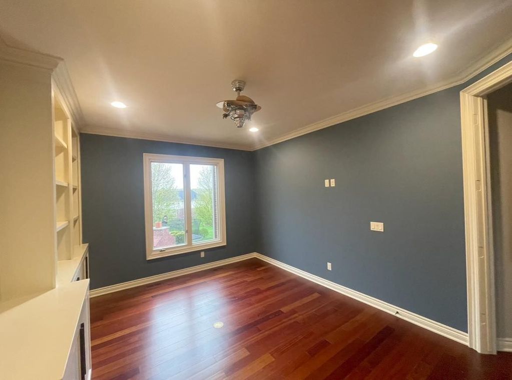 An empty room with hardwood floors , blue walls and a ceiling fan.