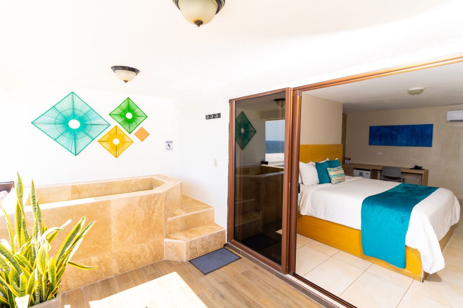 A hotel room featuring a private stone tub, decorative wall art, and a bed with blue and yellow accents.