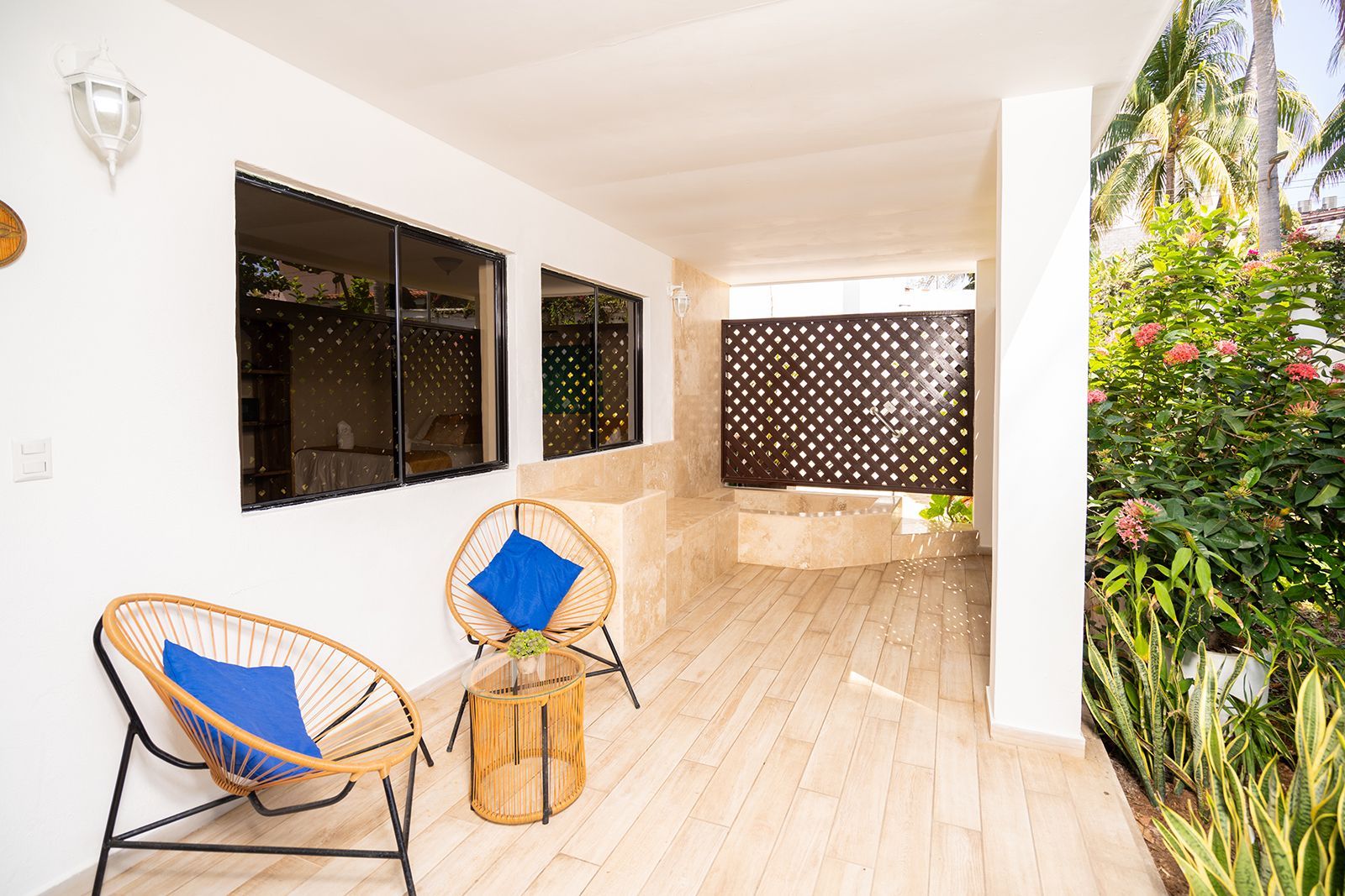 A covered patio with two woven lounge chairs, blue cushions, a small round table, and a decorative privacy screen.