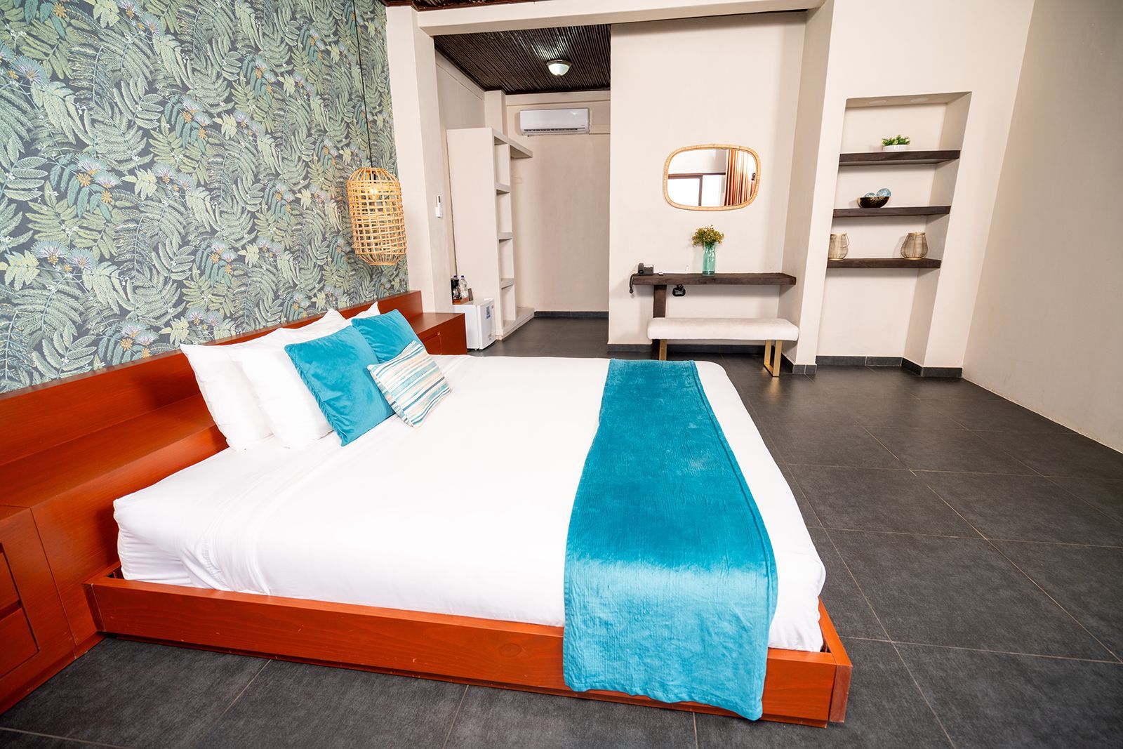 A hotel room with a king bed featuring white linens, a turquoise runner, and blue pillows against a patterned wall.