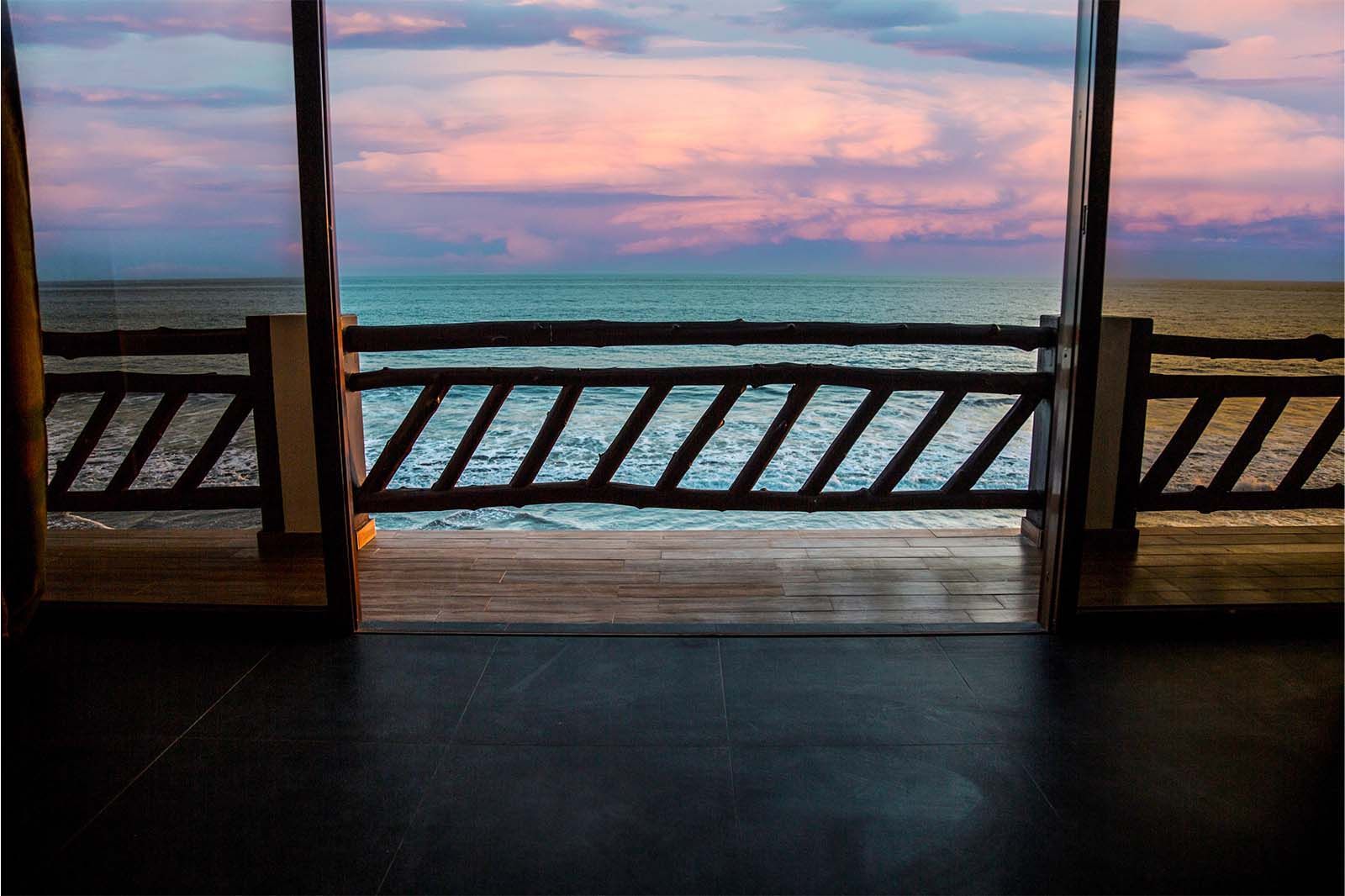 A wooden balcony overlooking the ocean at sunset with pink and blue clouds in the sky.
