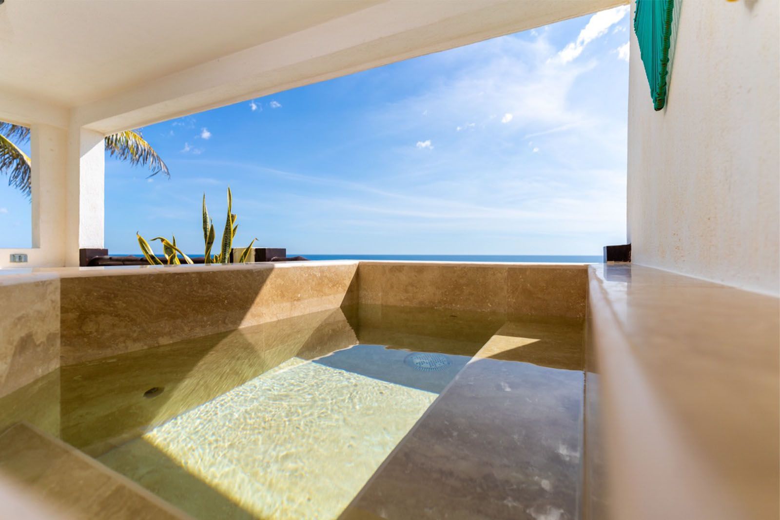 A shallow stone pool on a balcony overlooking the ocean under a bright blue sky.