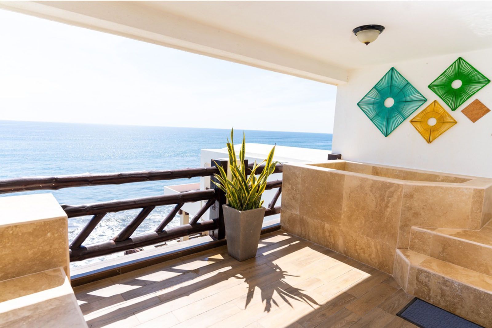 A stone terrace with a built-in tub and potted plant overlooking the ocean, decorated with colorful diamond wall hangings.