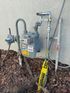 A gas meter is sitting next to a pipe on the side of a building.