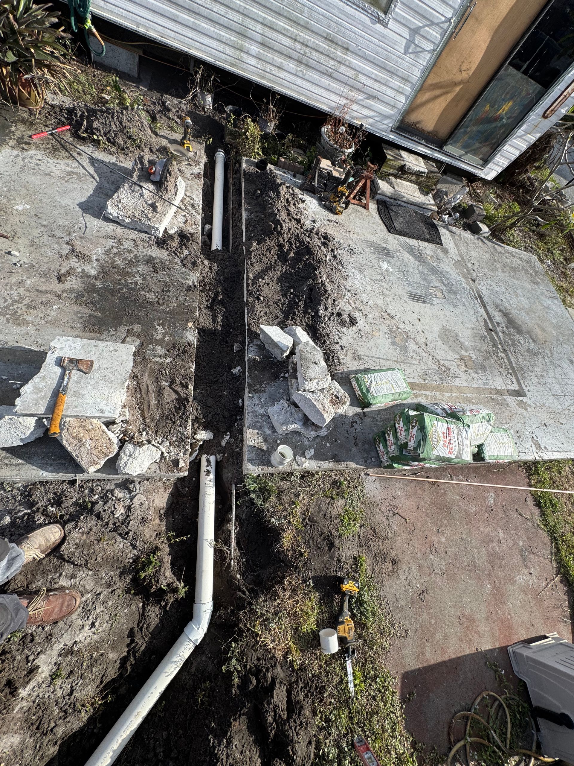 A drain pipe is being installed in the dirt in front of a house.