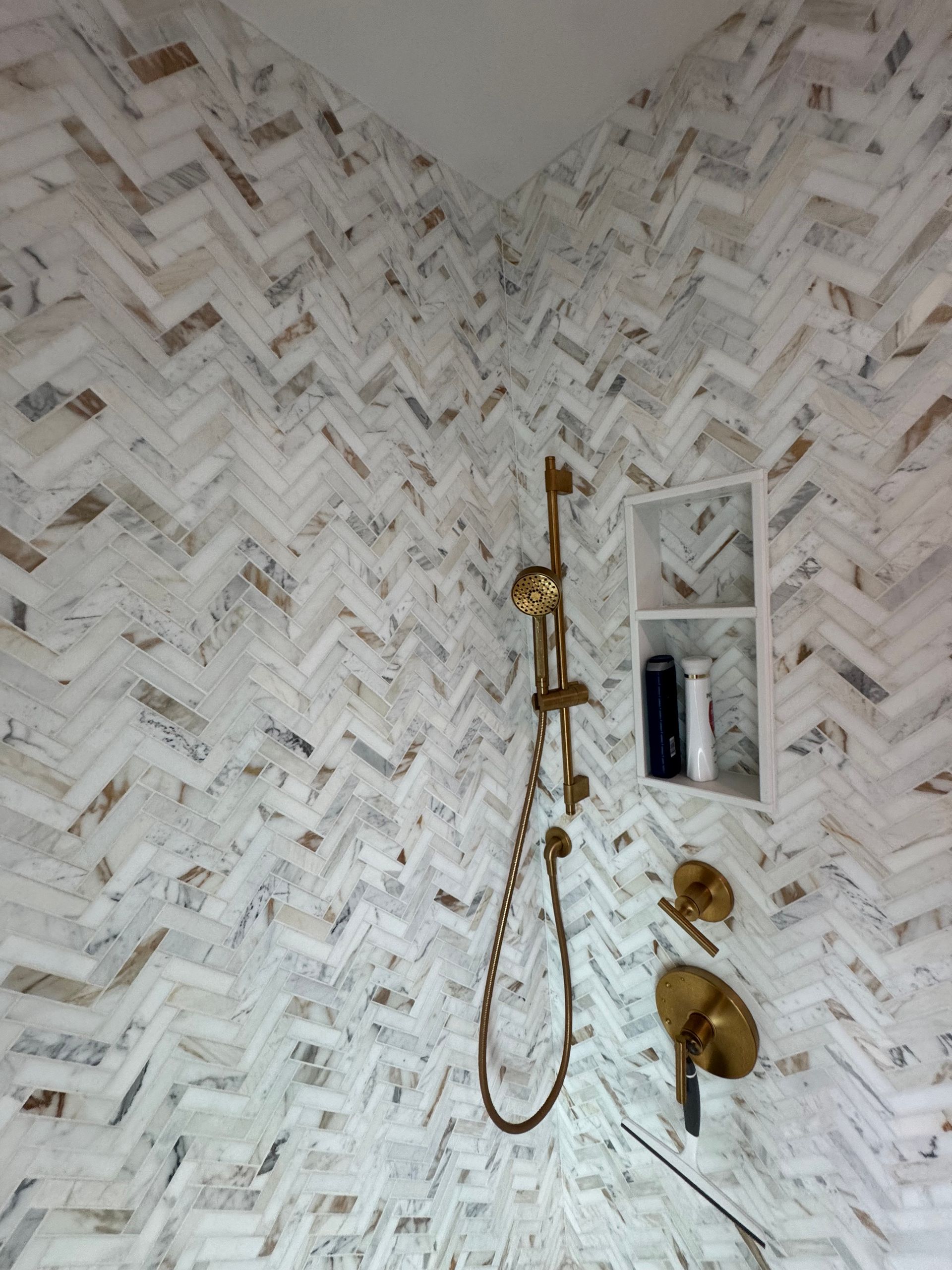 A shower with a herringbone pattern and a brass shower head