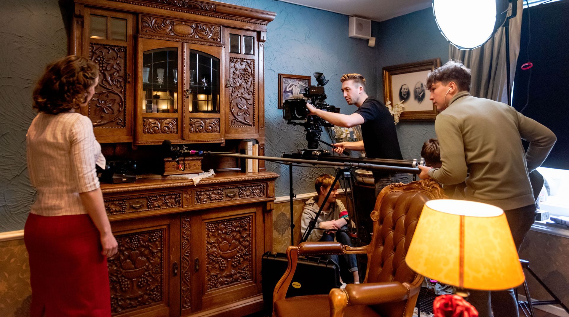 Een filmploeg filmt een vrouw die voor een sierlijke houten kast staat in een studio.