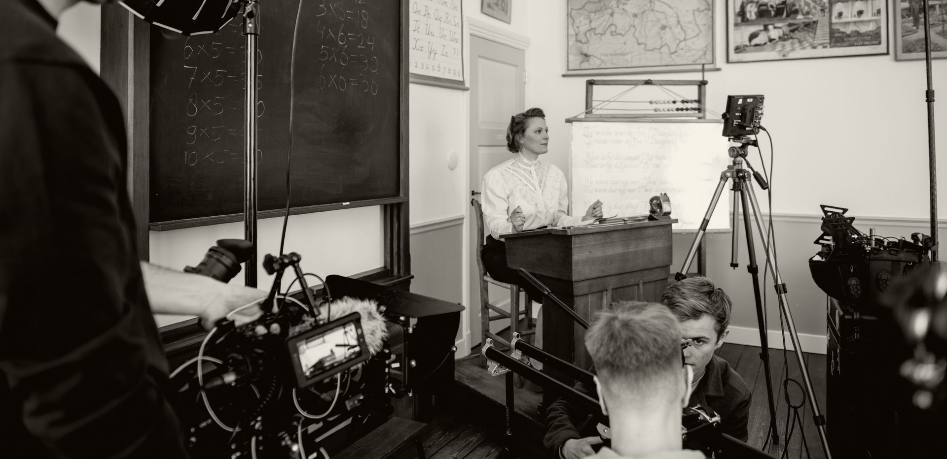 Een kijkje achter de schermen bij een filmploeg die een persoon filmt die aan een bureau in een klaslokaal zit.
