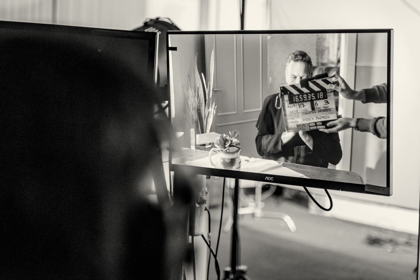 Een persoon zit achter een filmklapper voor een monitor waarop een zwart-witbeeld van hem of haar op de set te zien is.