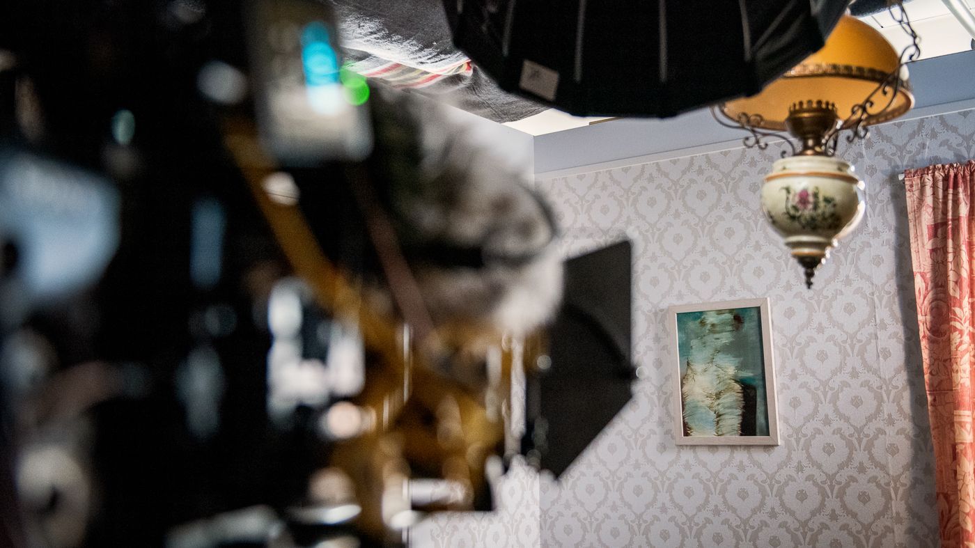 Een professionele camera-opstelling is gericht op een muur met behang met een patroon, een ingelijst portret en een vintage hanglamp.