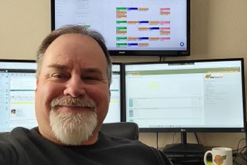 A man with a beard is sitting in front of two computer monitors.