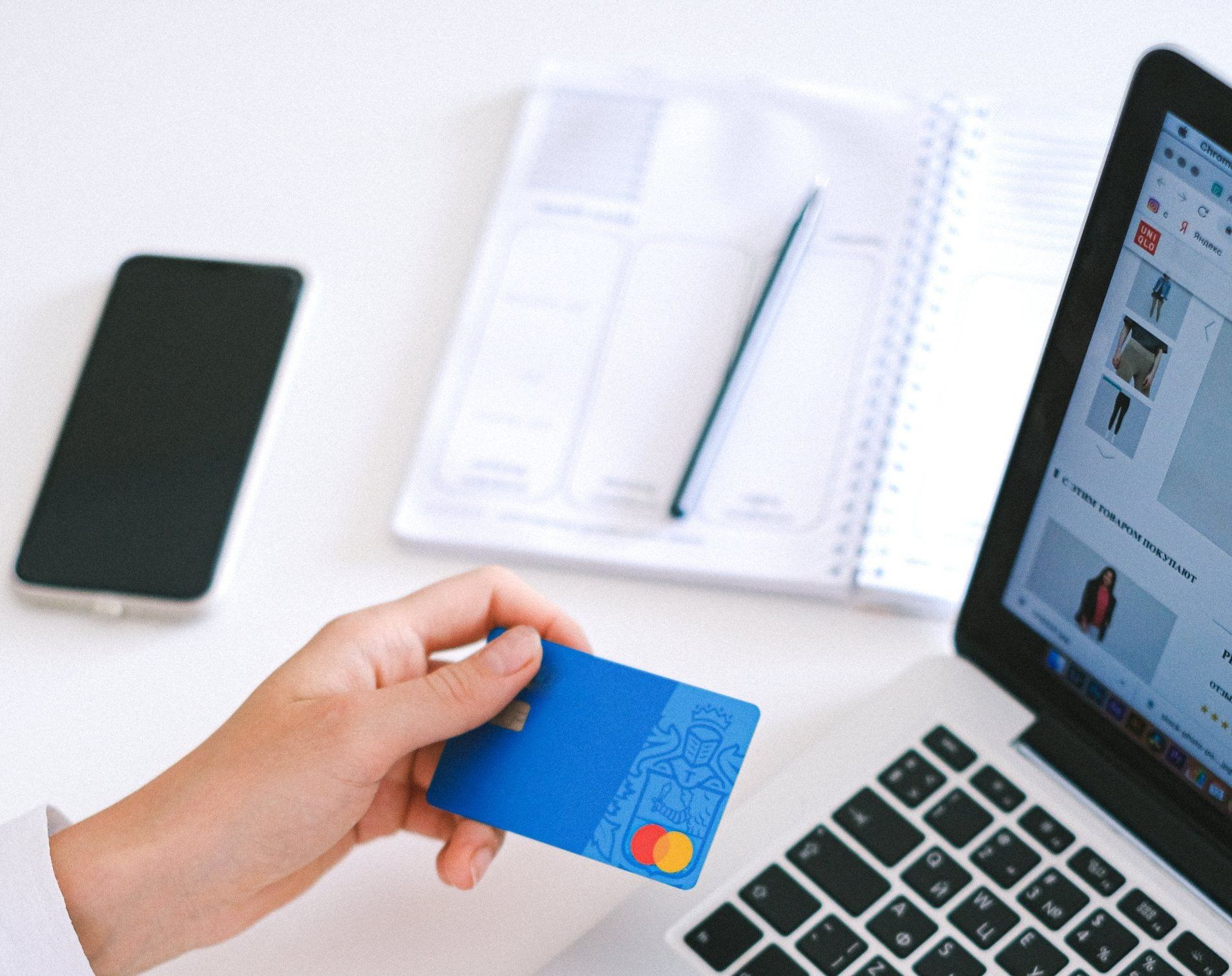 A person is holding a credit card in front of a laptop