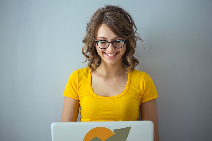 A woman wearing glasses is smiling while using a laptop computer