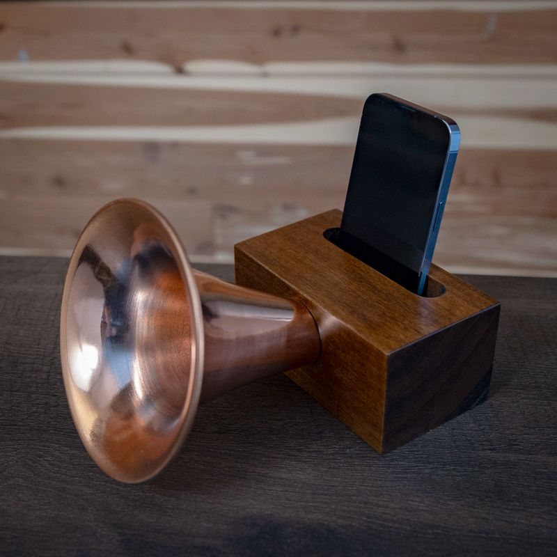 A copper trumpet sits on a wooden box with a cell phone in it