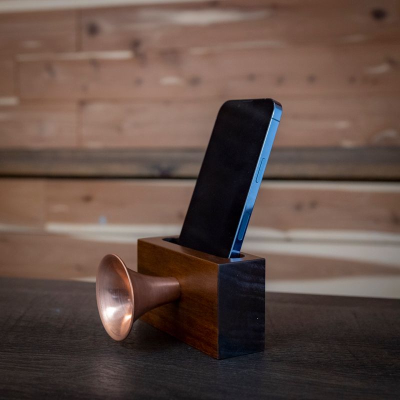 A phone is sitting in a wooden box with a copper horn attached to it
