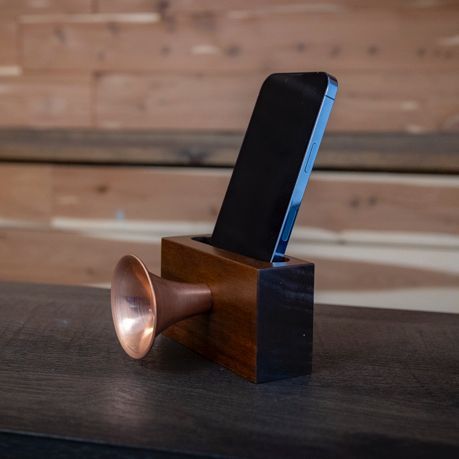 A phone is sitting in a wooden holder with a copper horn attached to it