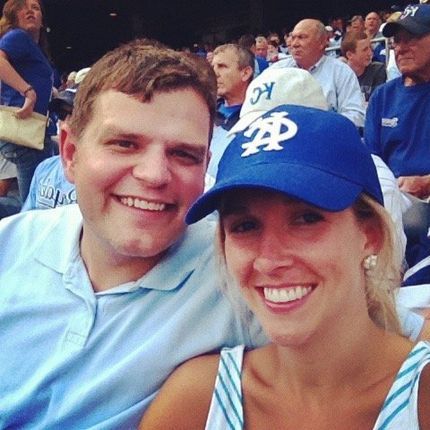 A man and a woman are posing for a picture and the woman is wearing a kc hat