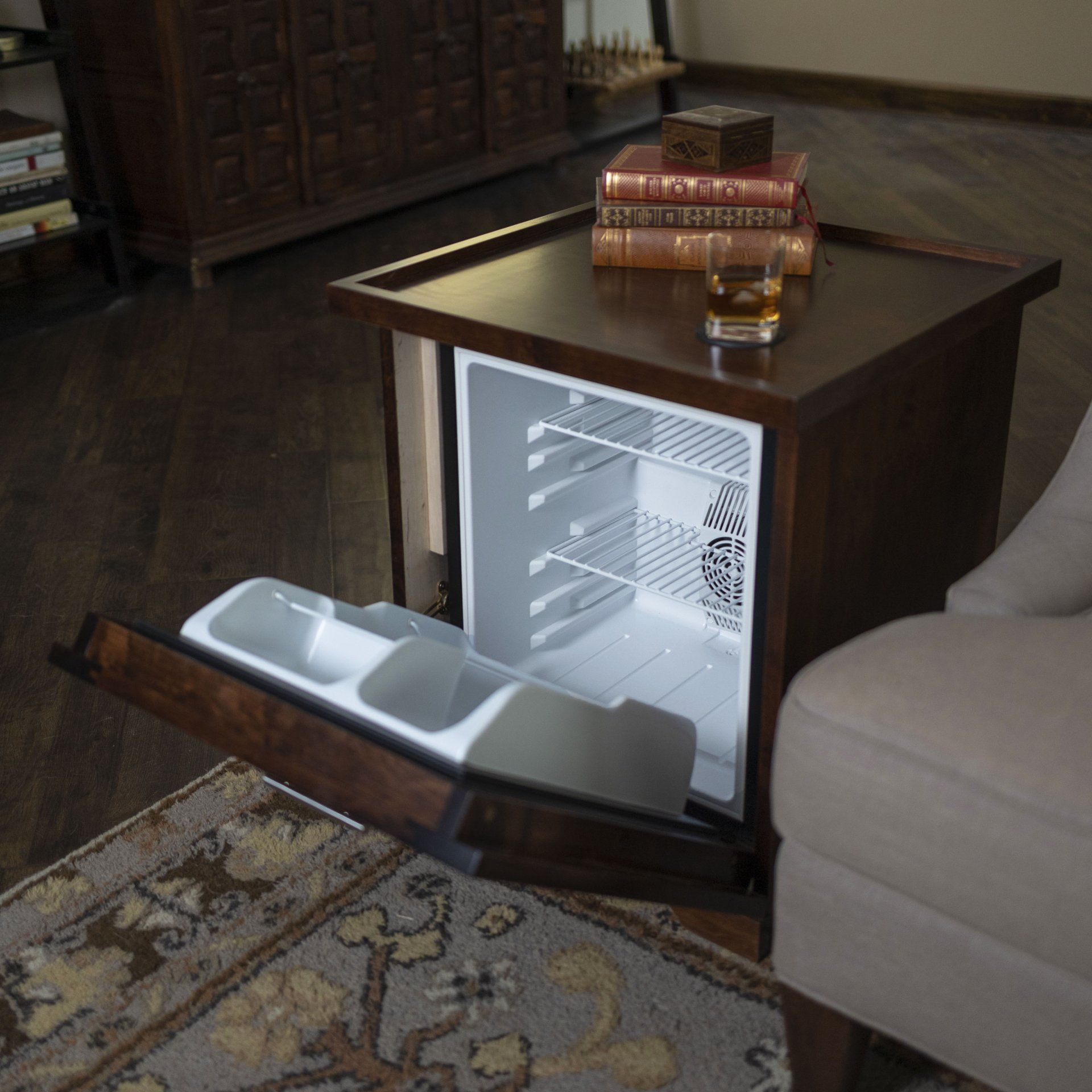A small fridge sits on a table next to a chair