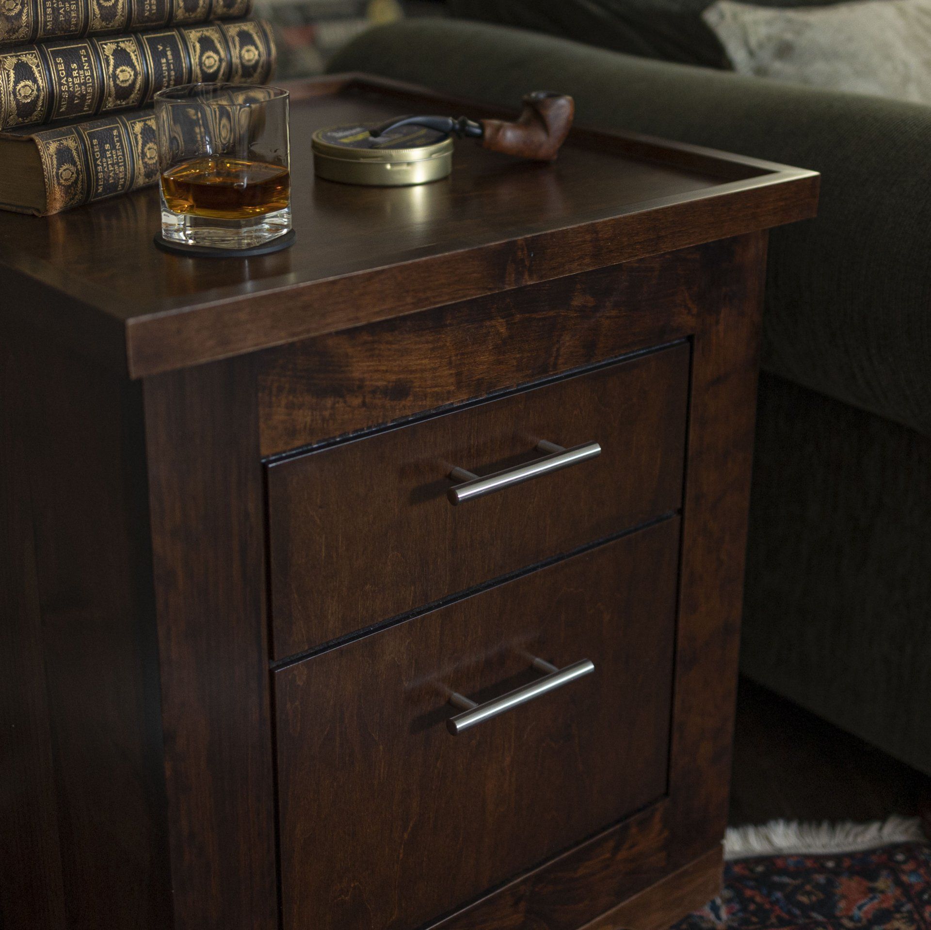 A nightstand with a glass of whiskey and a pipe on it