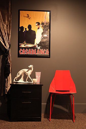 A red chair is sitting next to a nightstand and a poster on the wall.