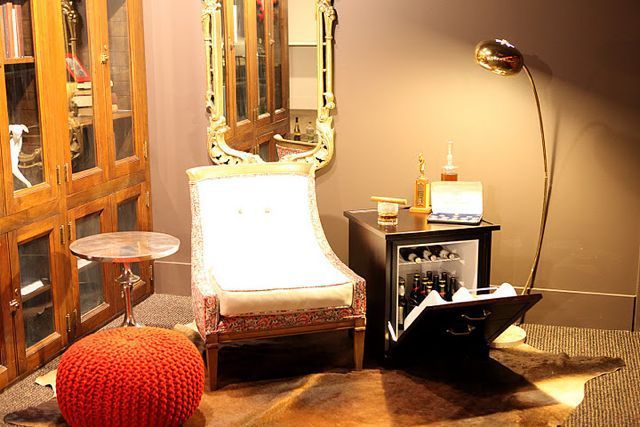 A living room with a chair , ottoman , lamp and mirror.