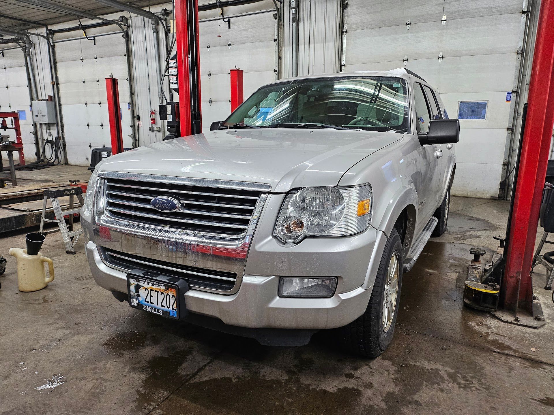 A silver Ford Explorer SUV parked inside a vehicle maintenance shop with red hydraulic lift posts. | Aurora Automotive