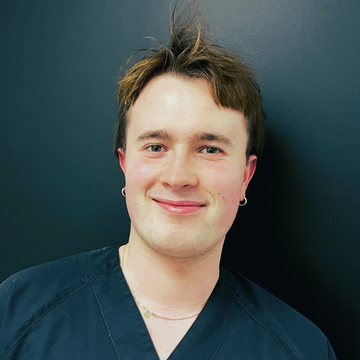 Tannlege Christian med briller og skjegg, iført blå skjorte og medisinsk maske, smiler til kameraet.