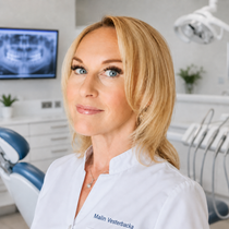Smilende tannlege Madel Holmedal Gjerding, i hvit frakk med stetoskop på et klinikkkontor.