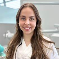 Smilende tannlege Madel Holmedal Gjerding, i hvit frakk med stetoskop på et klinikkkontor.