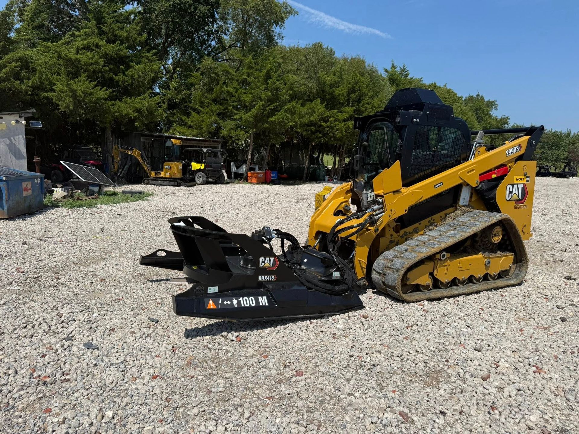 Yellow skid steer loader with a black attachment on gravel, outdoors.