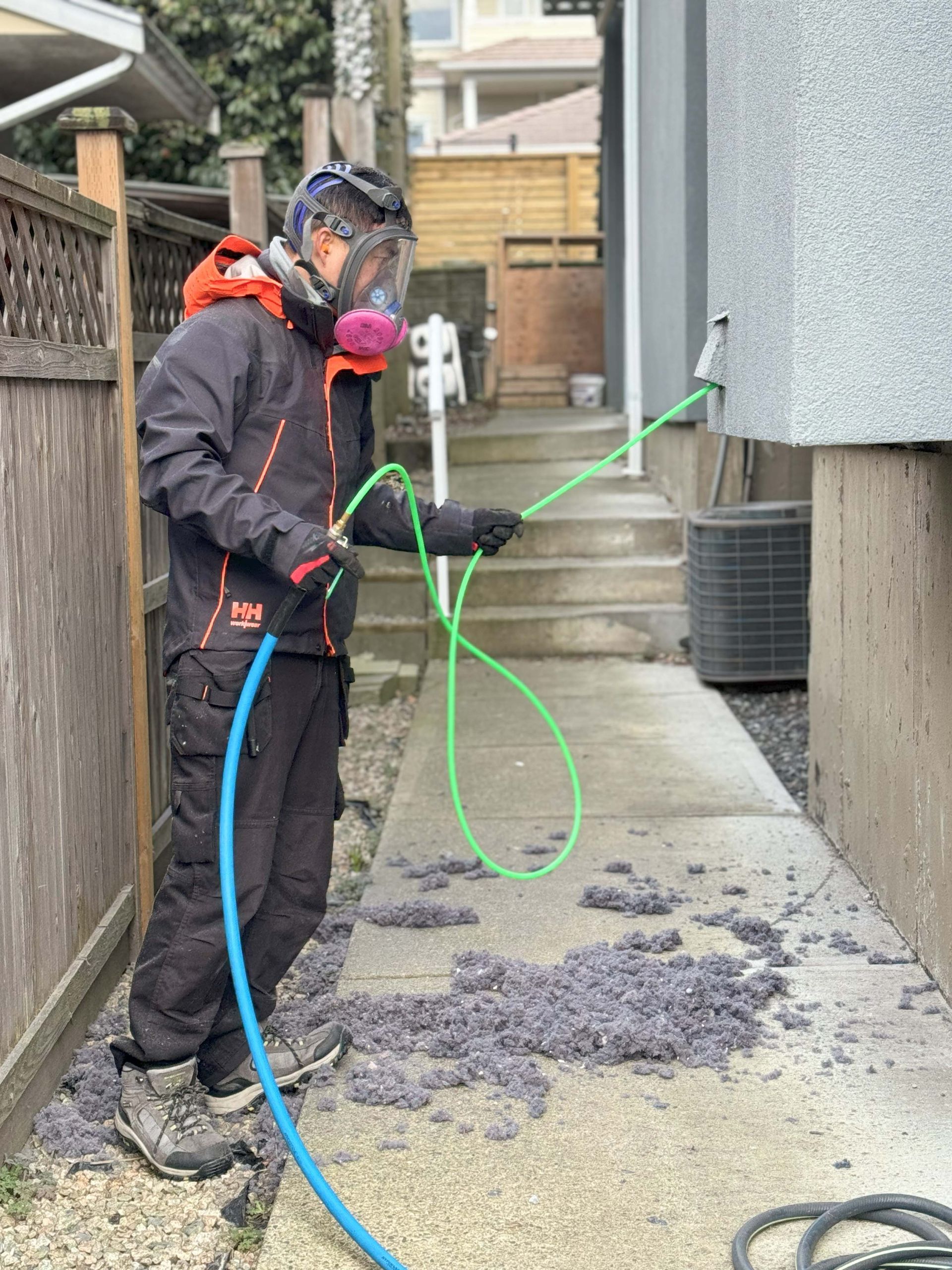 A man wearing a gas mask is spraying something with a hose.