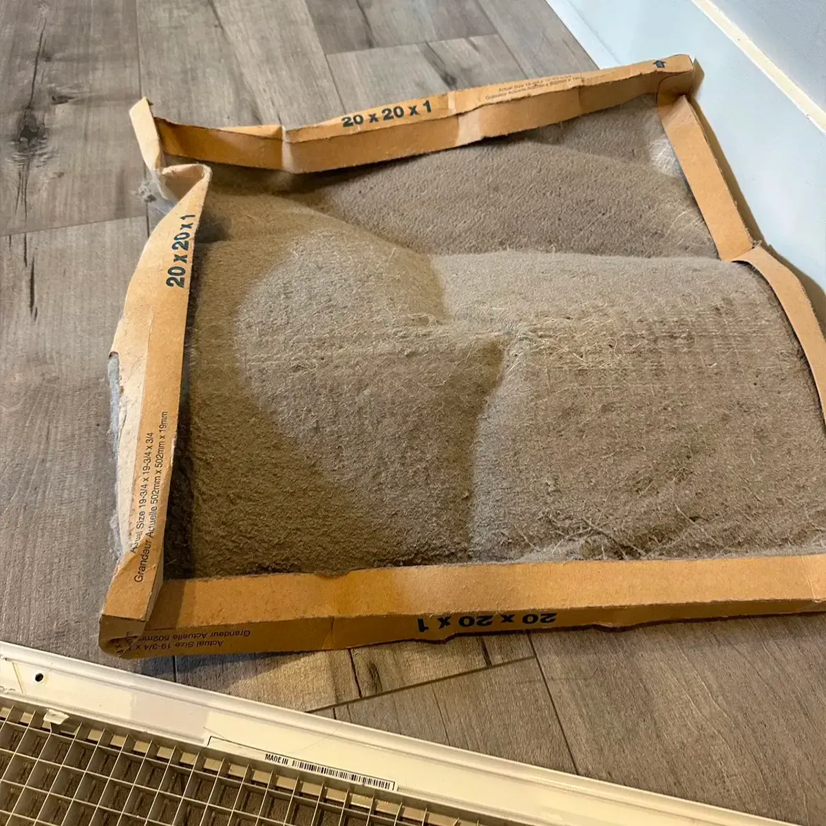 A cardboard box filled with sand is sitting on a wooden floor.