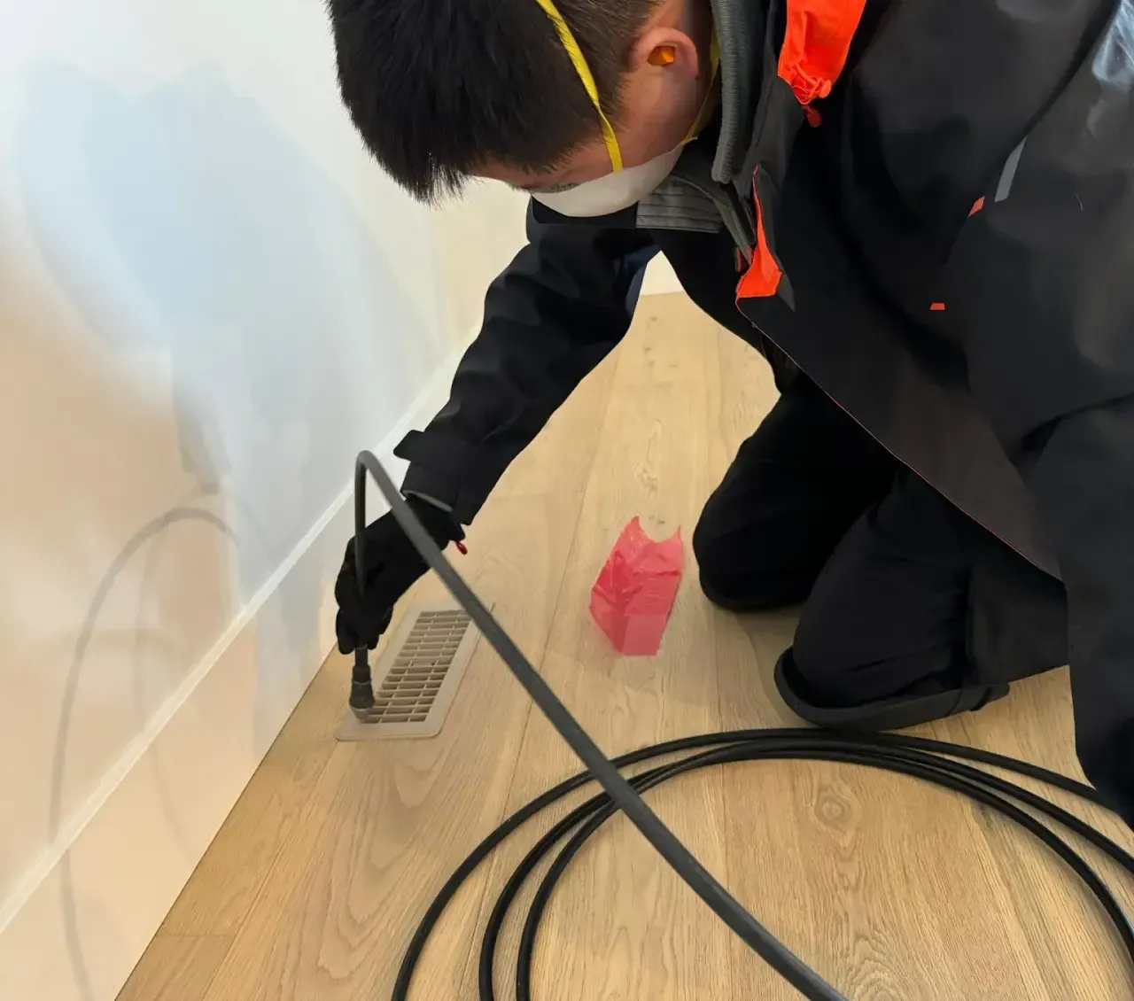 A man wearing a mask is kneeling down on the floor using a tool.