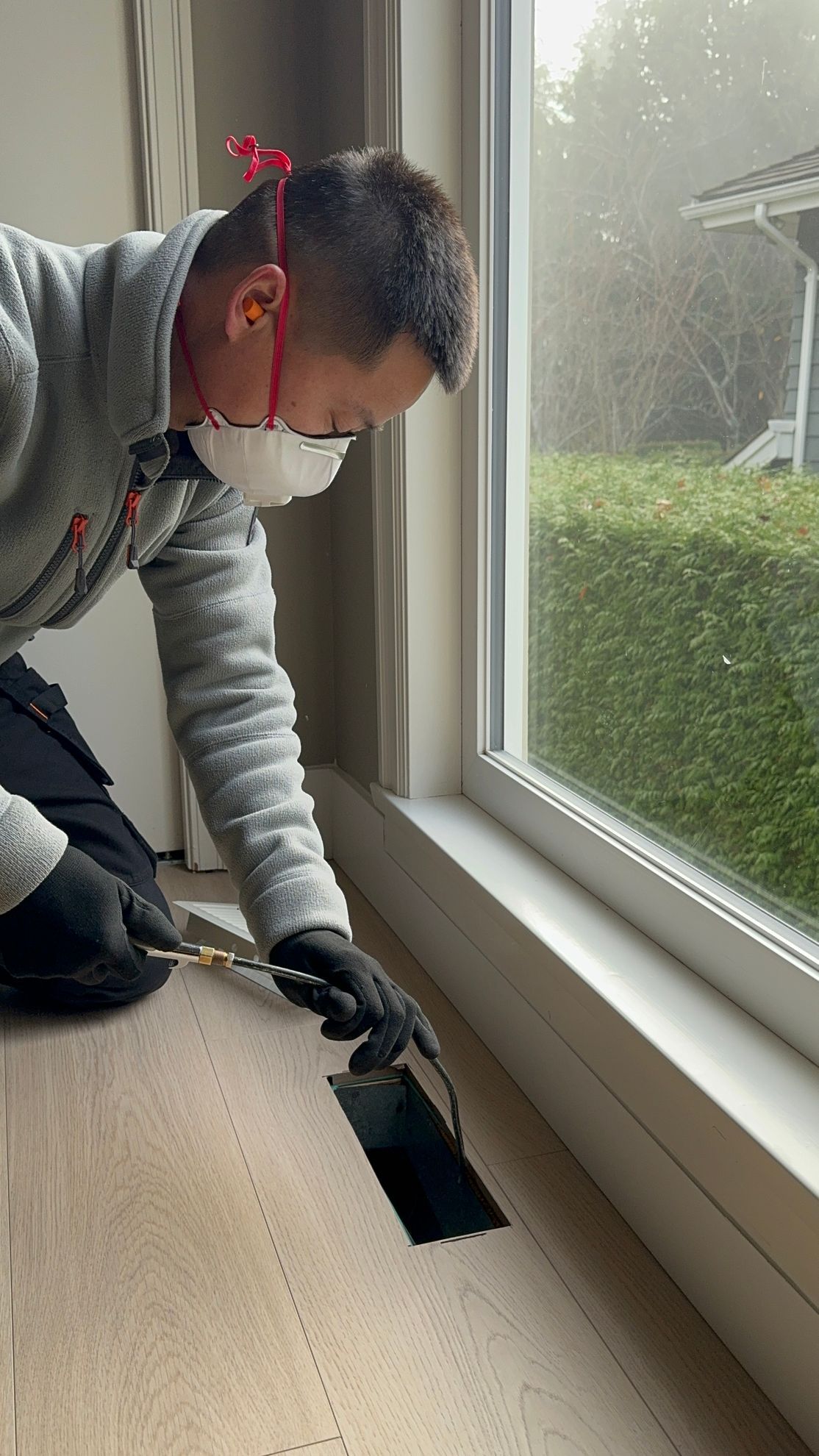 A man wearing a mask is kneeling down in front of a window.