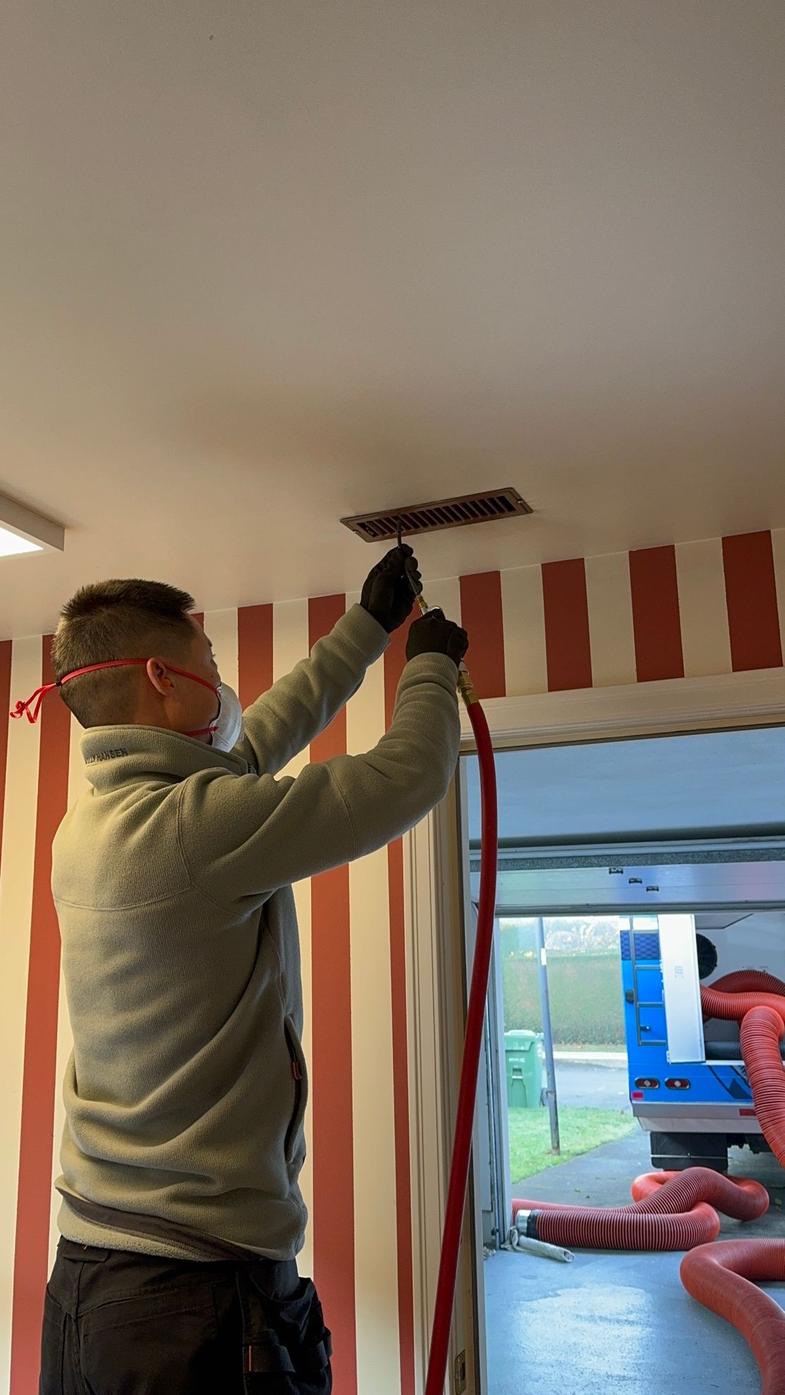 A man wearing a mask is working on a ceiling vent.