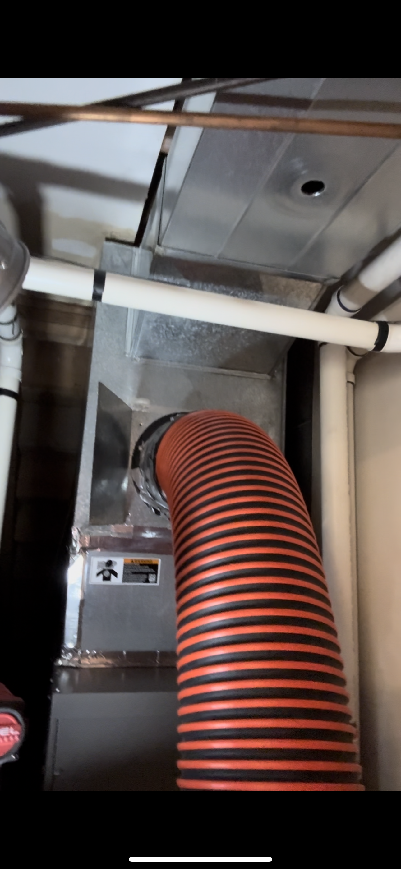 A red hose is coming out of a furnace in a basement.