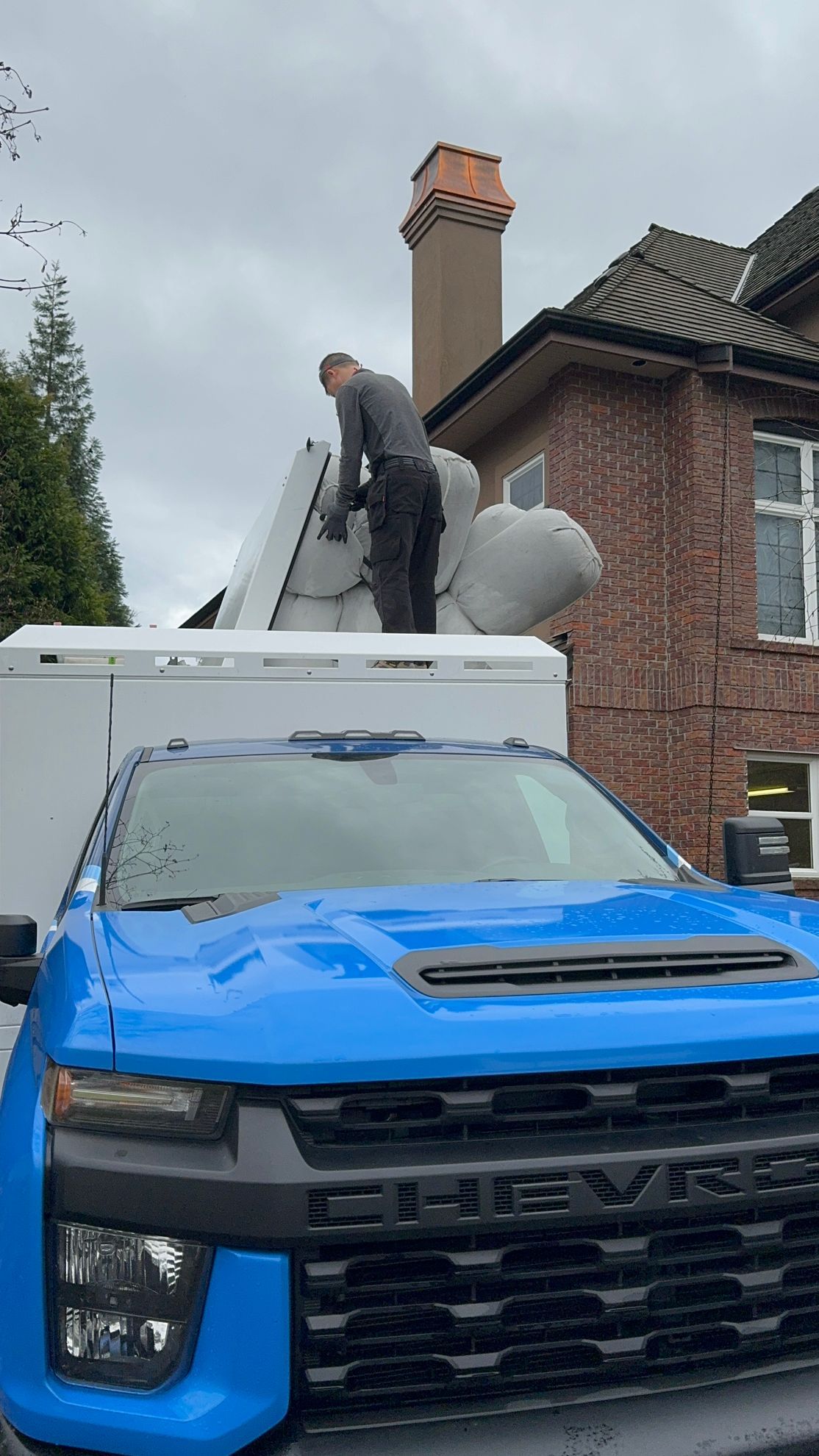 A man is standing on top of a blue truck in front of a house.