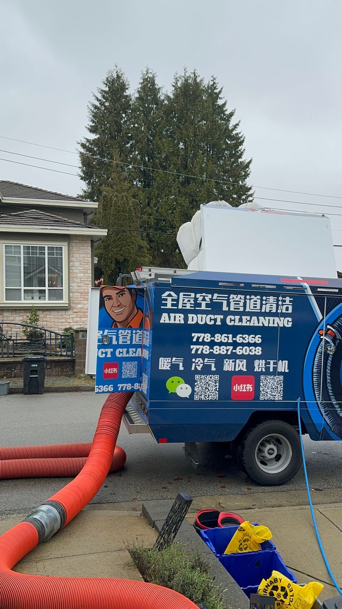 A blue air duct cleaning truck is parked in front of a house.