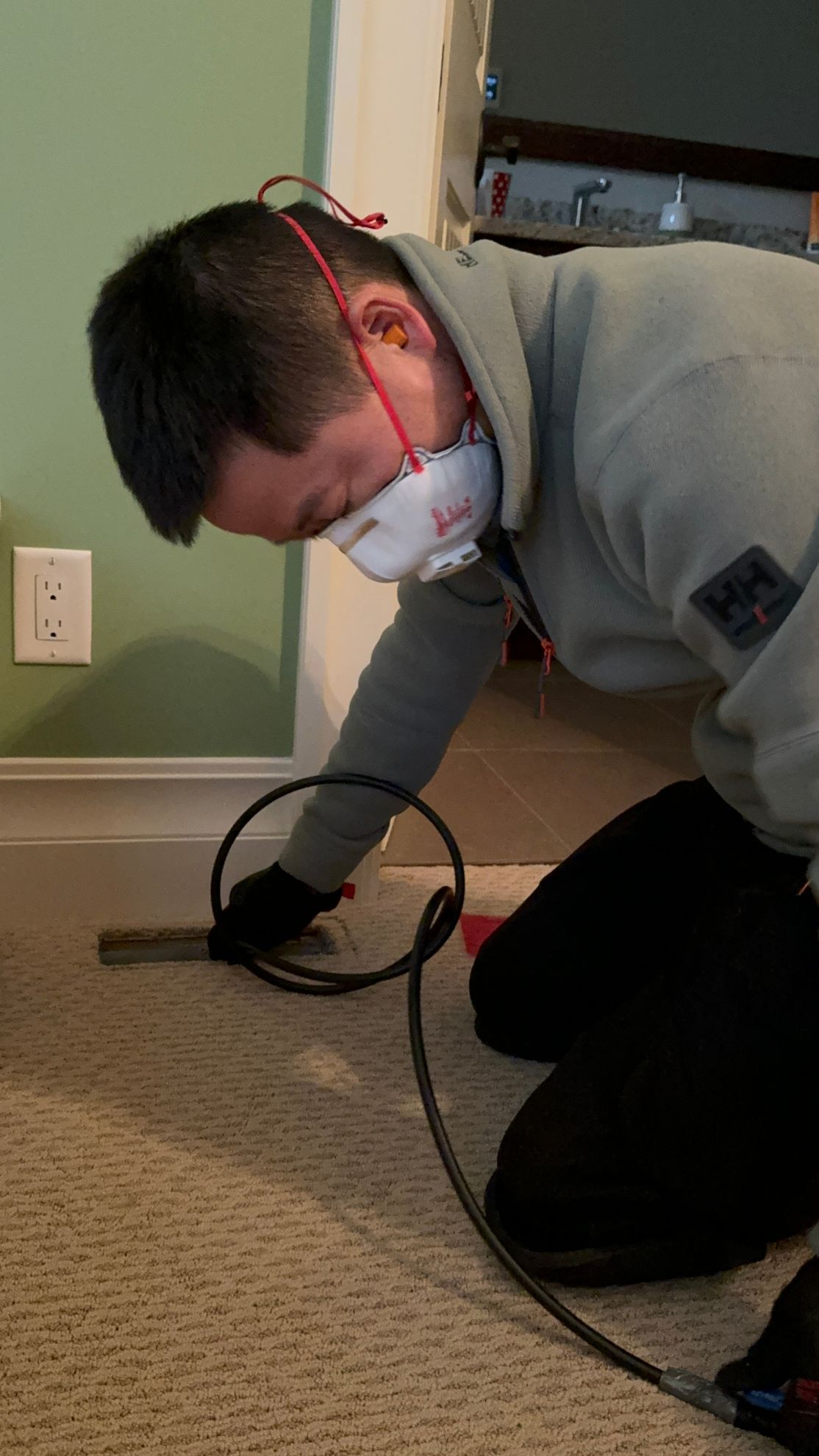 A man wearing a mask is kneeling on the floor using a machine.