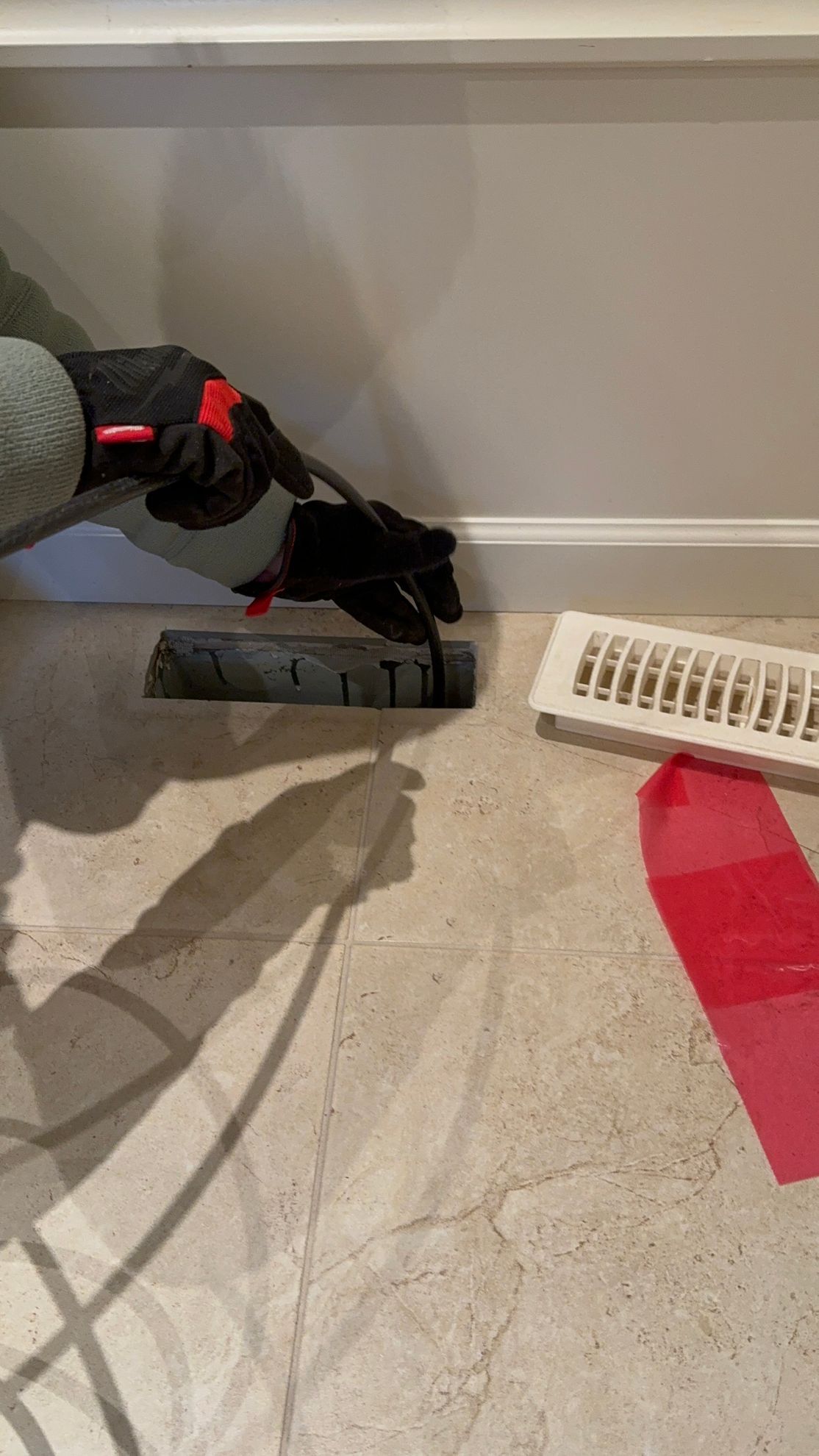 A person is cleaning an air vent with a vacuum cleaner.