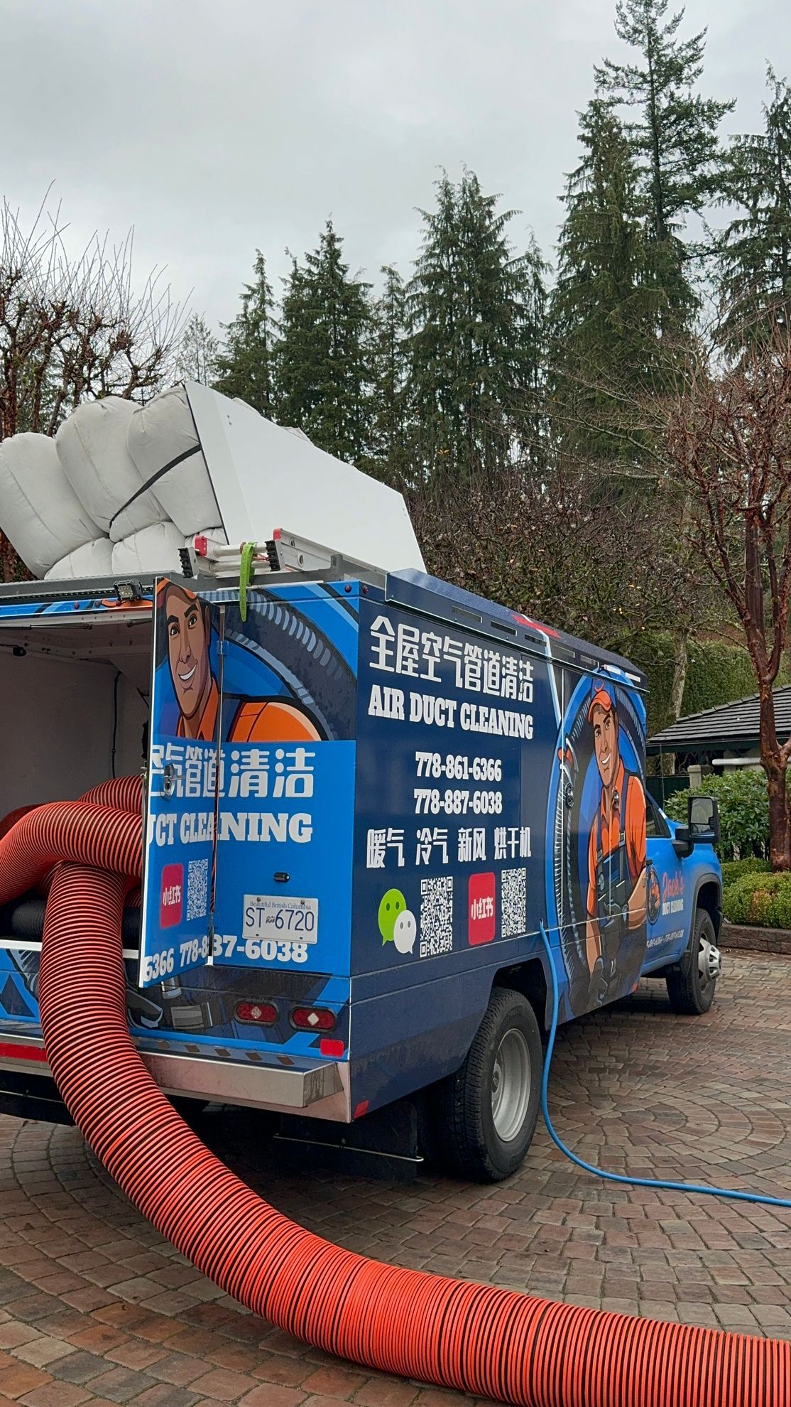 A blue truck with a red hose attached to the back is parked in a driveway.