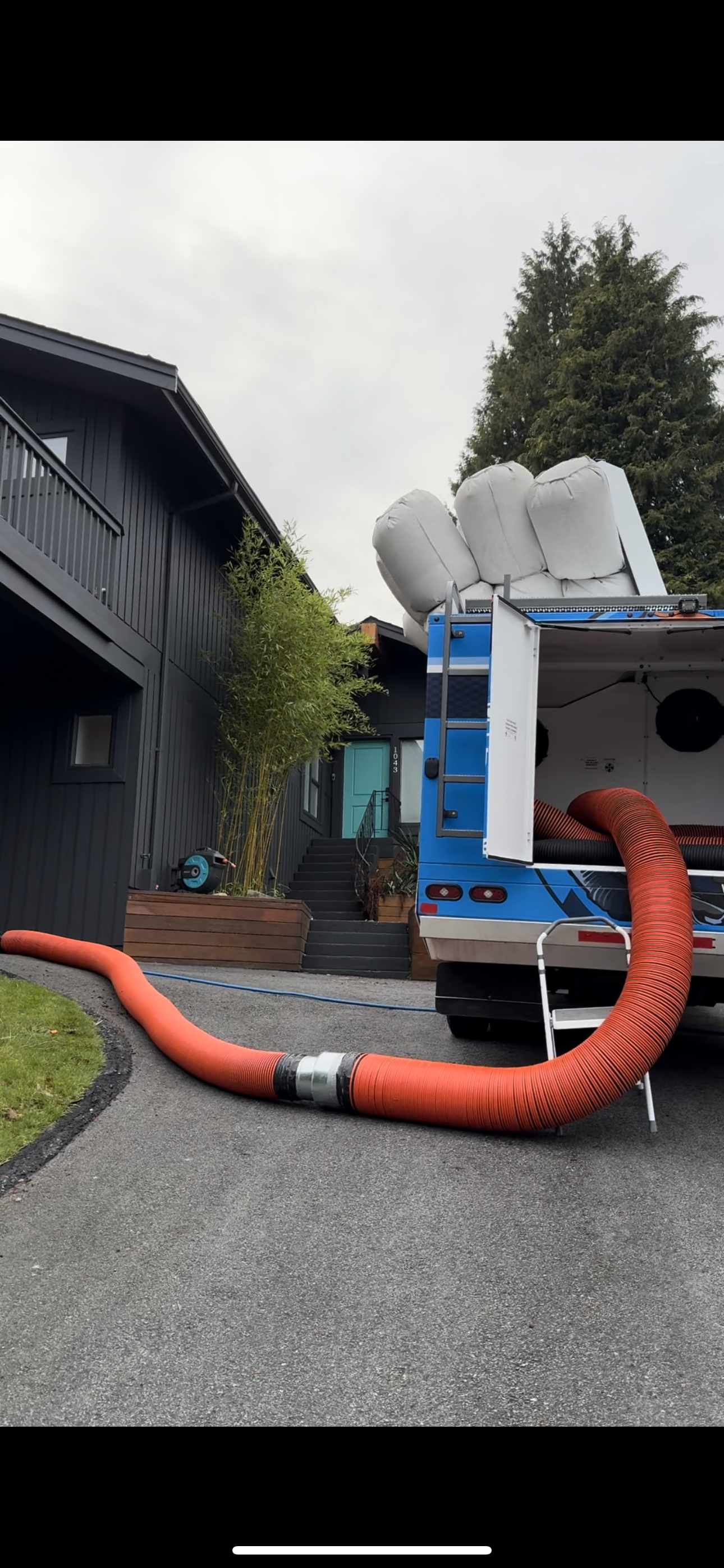 A truck with a hose attached to it is parked in front of a house.